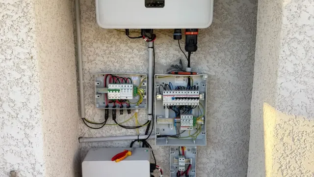Onduleur blanc et coffrets électriques ouverts avec leurs protections, fixés dans une niche de façade crépie