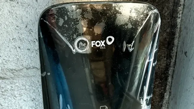 Gros plan sur la face avant noire et brillante d'une borne de recharge Fox ESS fixée sur un mur en béton