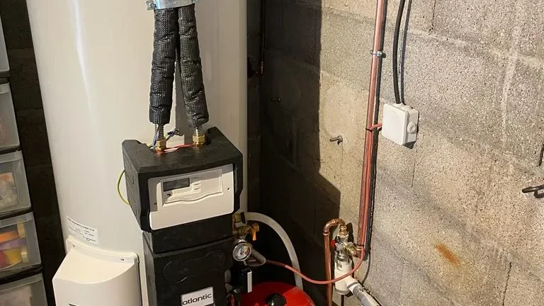 Ballon d'eau chaude avec module de régulation à écran et vase d'expansion rouge, contre un mur en parpaings