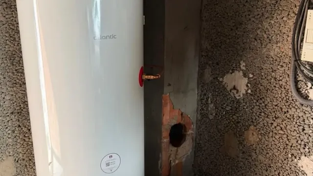 Ballon d'eau chaude blanc installé dans un local aux murs bruts, avec un raccord en cuivre sur le côté