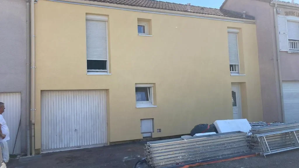 Façade enduite jaune d'une maison mitoyenne avec porte de garage, éléments d'échafaudage démontés posés devant
