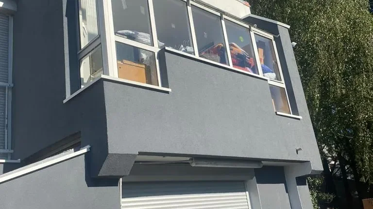 Façade enduite gris anthracite d'une maison avec une avancée vitrée à l'étage, au-dessus d'une porte de garage