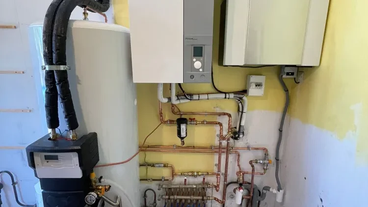 Module intérieur mural avec écran de réglage, ballon et tuyauteries en cuivre reliées à un collecteur dans un local technique